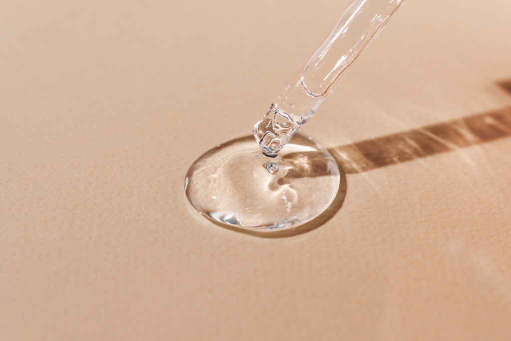 Klar gel som drypper fra en pipette ned på en beige flate